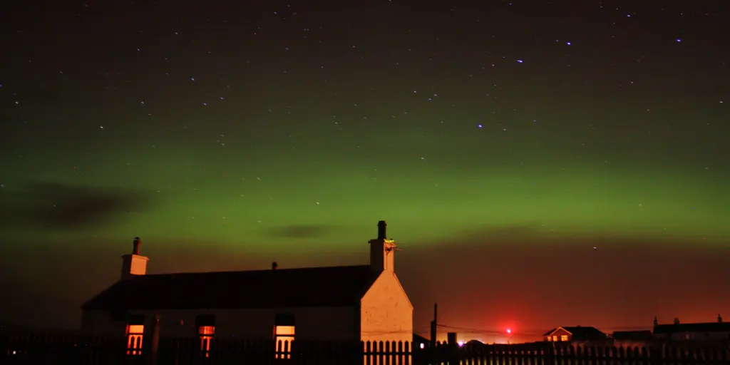 Red, green and purple Northern Lights visible in the sky above a silhouetted house in Scotland