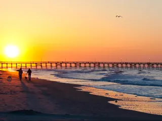 Sunset over Myrtle Beach, with people walking their dogs across the sand, towards the pier