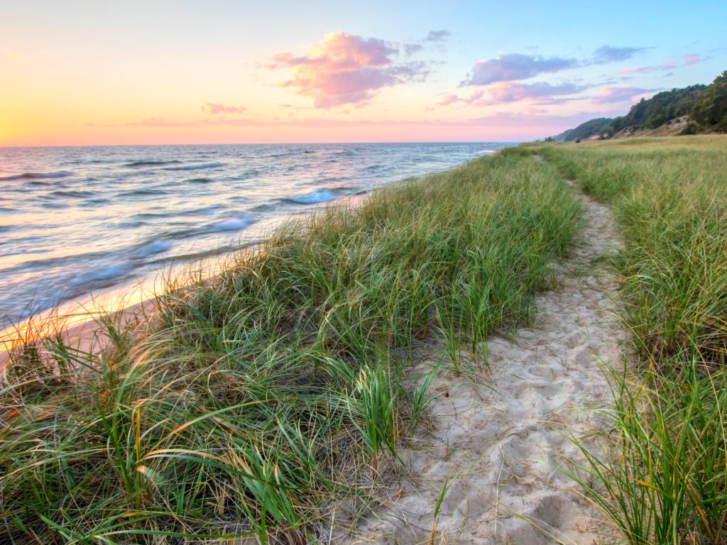 Lake Michigan, USA with a beach and a sandy path winding along the shore of Lake Michigan with a sunset horizon and sand dunes as a backdrop. 