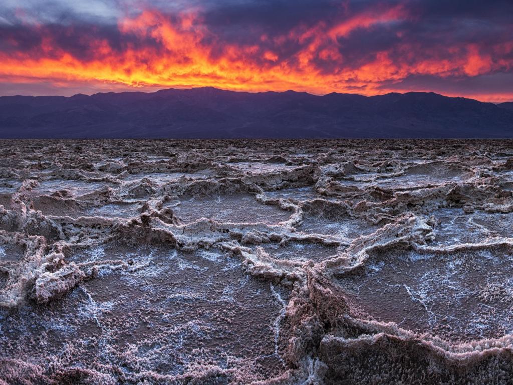 Death Valley National Park, California, USA with a fiery sunset over Badwater, the lowest point in the US and dried terrain in the foreground.