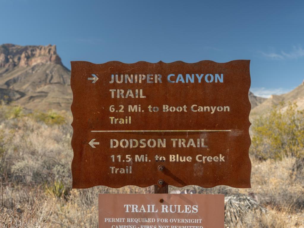 Close up view of brown signs highlighting Juniper Canyon And Dodson Trail Sign, against backdrop of parkland and blue skies