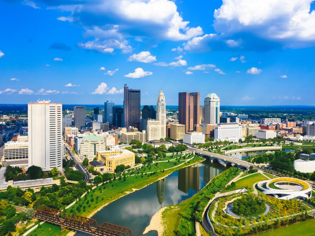 Aerial view of Downtown Columbus Ohio with Scioto River. The sky is blue with a few clouds and there is a park in the foreground of the photo.