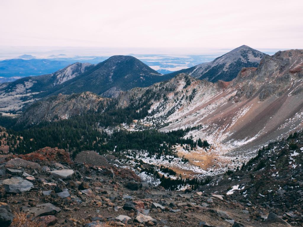 Humphrey's Peak, Arizona, with a rocky terrain in the foreground and snowcapped mountains in the distance in Winter with a hazy sky above.