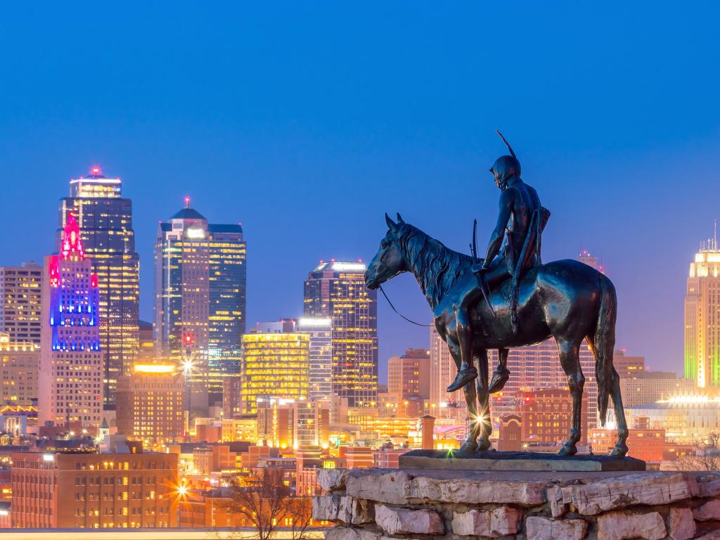 Statue of a man on horseback looking out over high rise buildings lit up at dusk