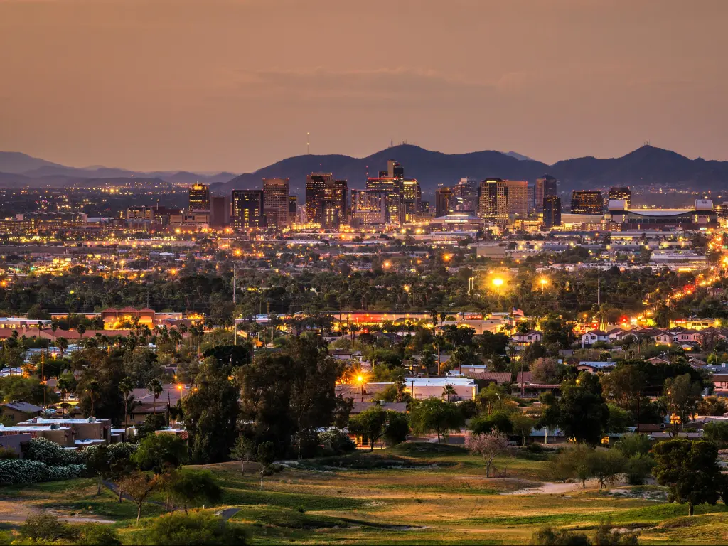 Phoenix, Arizona, USA with an aerial view of the city skyline at sunset with mountains in the distance. 
