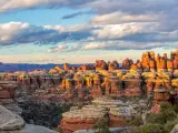 Moody clouds above golden lit needle-shaped rock formations looking out across wide canyon and deep valley
