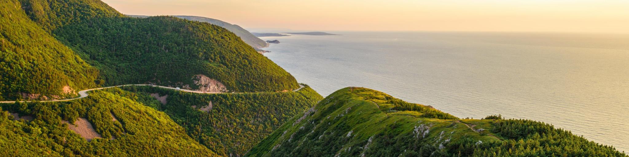 Cape Breton, Nova Scotia, Canada with green covered hills in the foreground hills Skyline looking to a valley below and beyond that the sea on a sunny day.