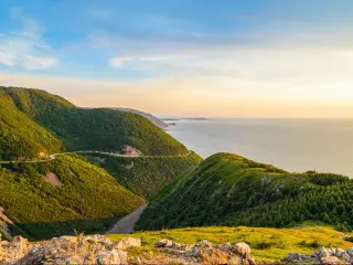 Cape Breton, Nova Scotia, Canada with green covered hills in the foreground hills Skyline looking to a valley below and beyond that the sea on a sunny day.