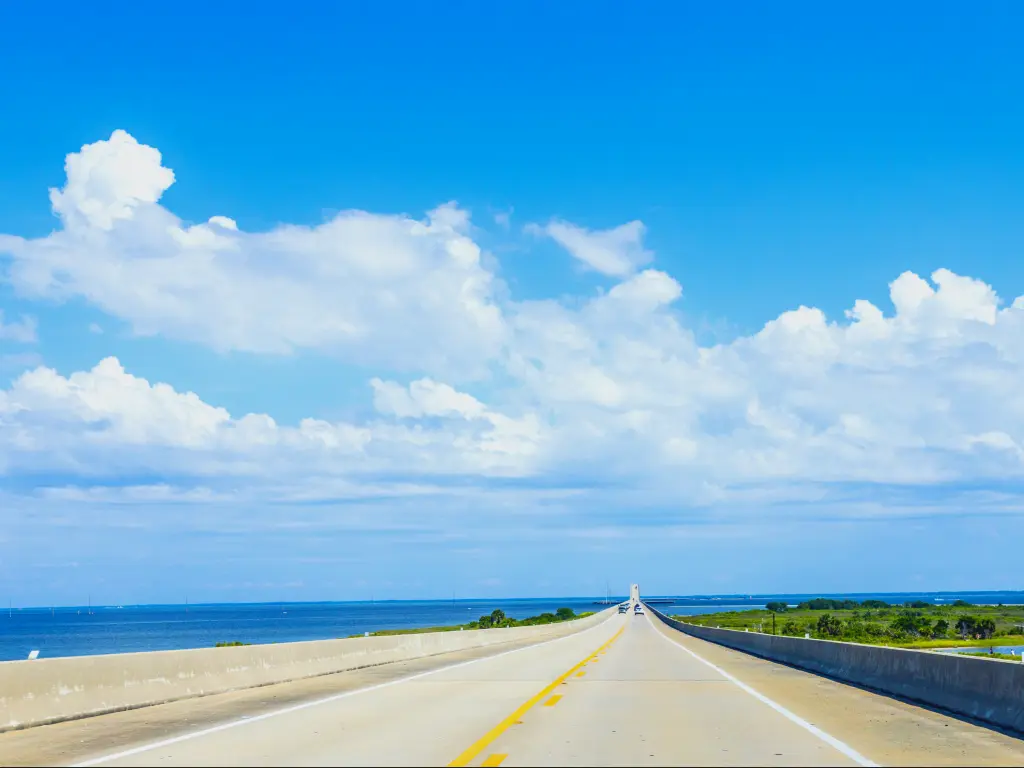 Cars driving along Interstate 193 in Gordon Persons Bridge with a scenic view of Mobile Bay on a sunny day with a thick white blanket of stretched out cotton clouds