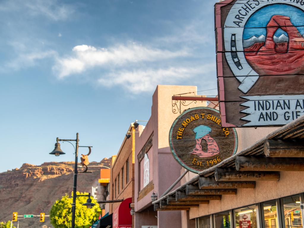 Moab, Utah, USA with street shop signs at sunset and mountains in the distance.