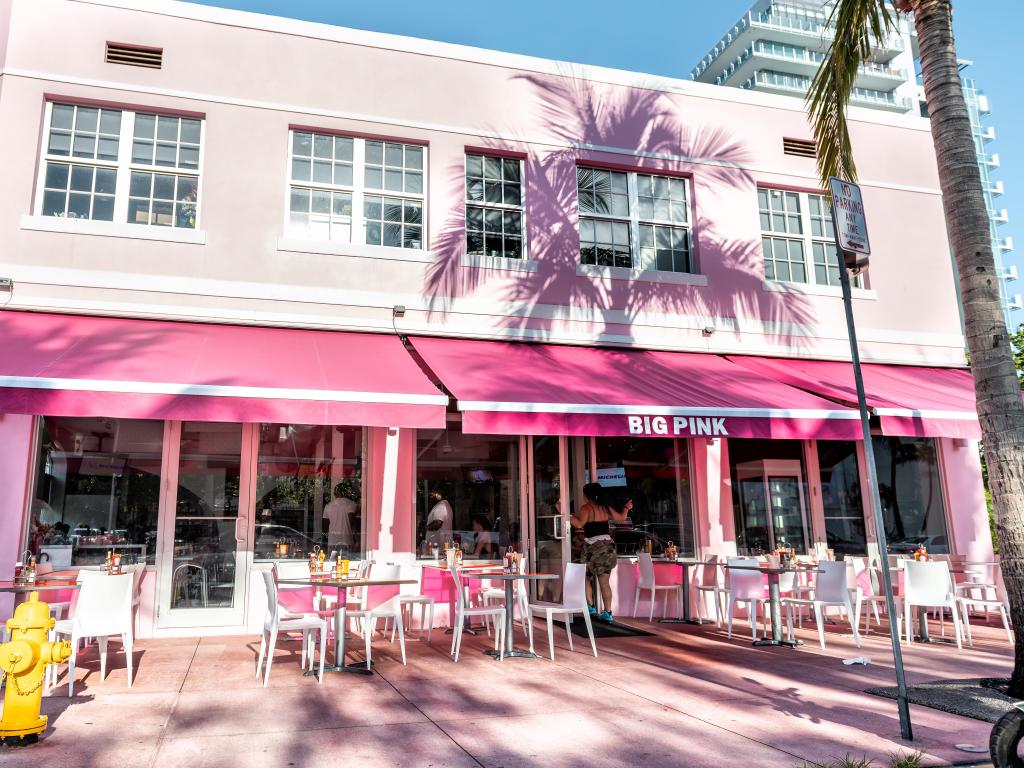 Sunny day, the view in front of the pink-colored diner with outside sitting empty area, tables, chairs