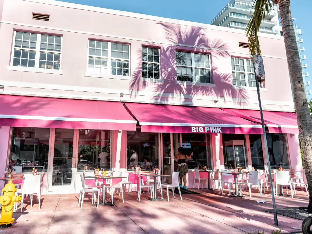 Sunny day, the view in front of the pink-colored diner with outside sitting empty area, tables, chairs