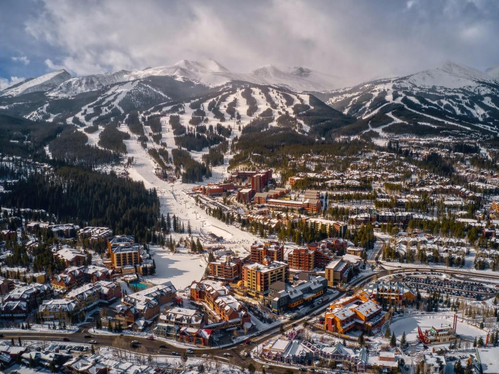 Breckenridge, Colorado, USA with an aerial view of the ski town and snow-capped mountains in the distance under low hanging cloud.