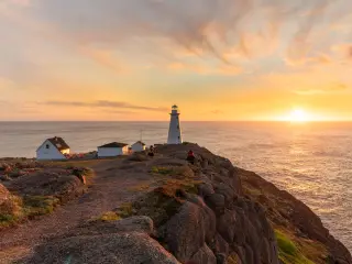 Beautiful sunrise over a white lighthouse sitting at the edge of a rocky cliff.