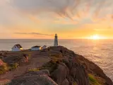 Beautiful sunrise over a white lighthouse sitting at the edge of a rocky cliff.