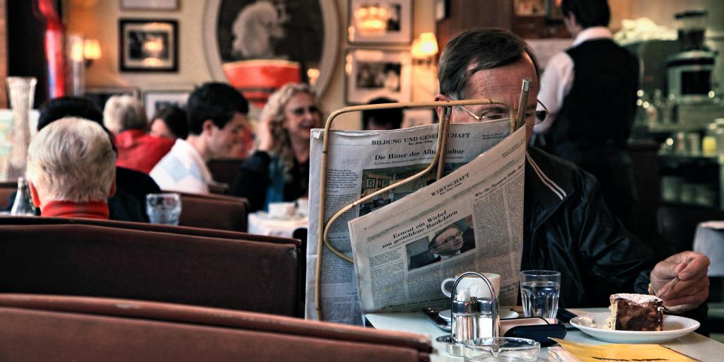 A man reading the newspaper and eating cake in a Vienna coffeehouse