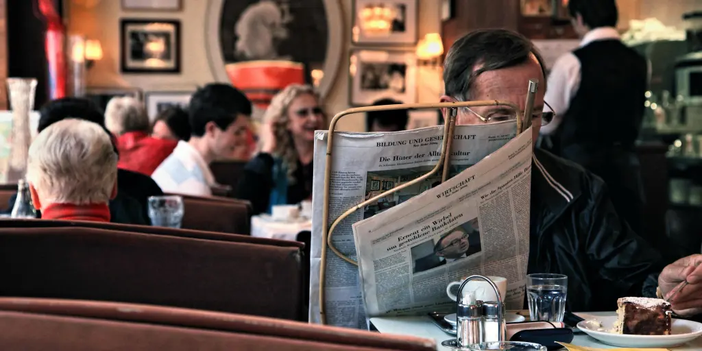 A man reading the newspaper and eating cake in a Vienna coffeehouse