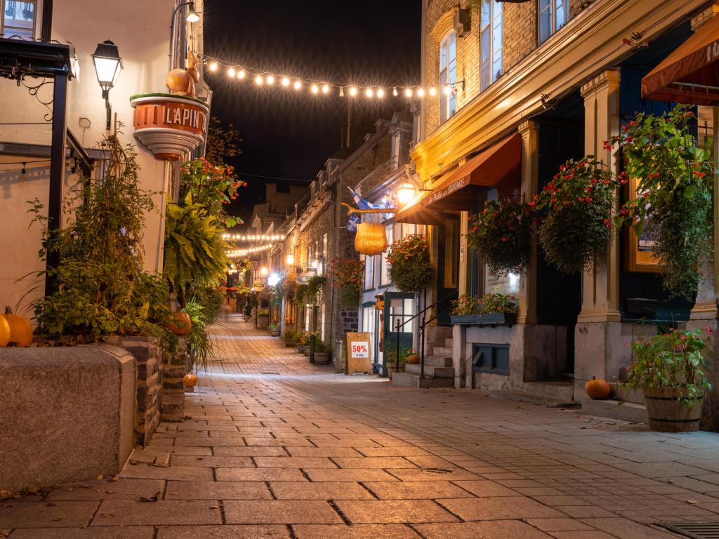 Quebec, Canada with a night view of the Quartier du Petit Champlain in fall with pretty shops either side of a cobbled street.