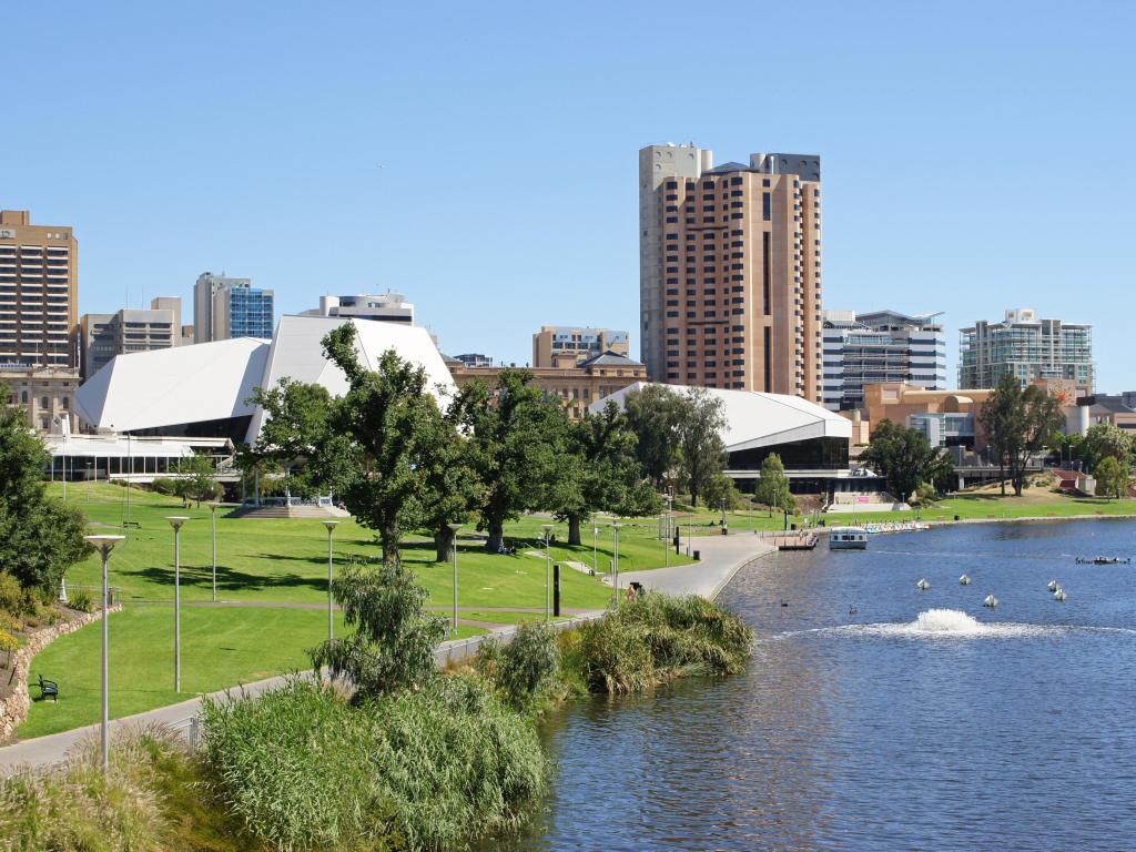 Adelaide, Australia with a panorama of the city on a sunny day with the river in the foreground and buildings in the background.