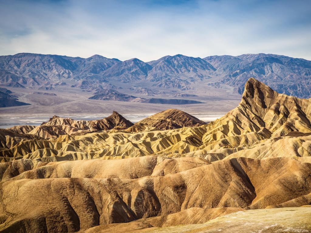 Death Valley National Park, California, USA taken on a sunny day with yellow rock formations in the foreground and mountains in the distance. 