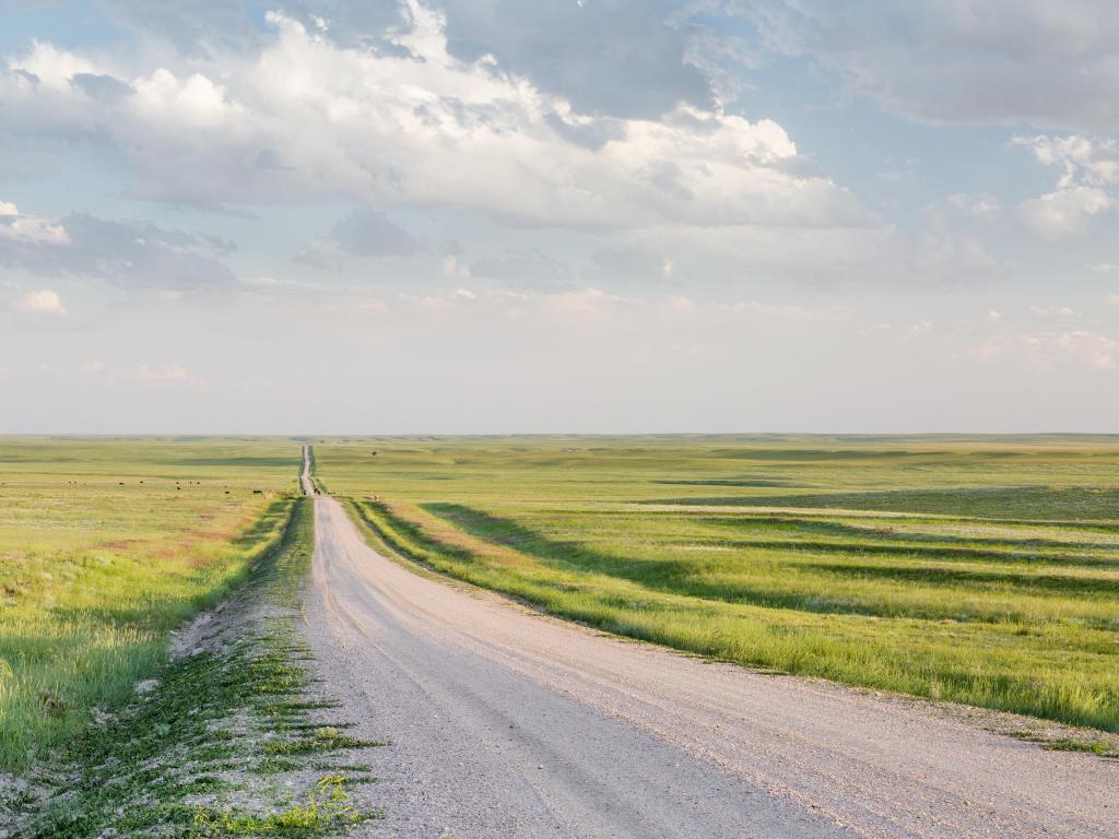 A rural road in eastern Colorado prairie in springtime, Pawnee National Grassland. The weather is cloudy with some blue peeking through. 