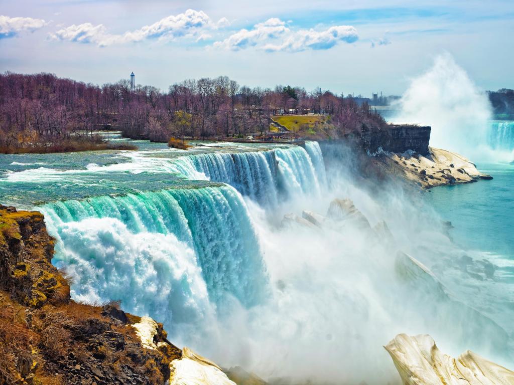 Niagara Falls, Niagara State Park view from the American side in spring with the waterfall creating spray against the rocks below on a sunny day.