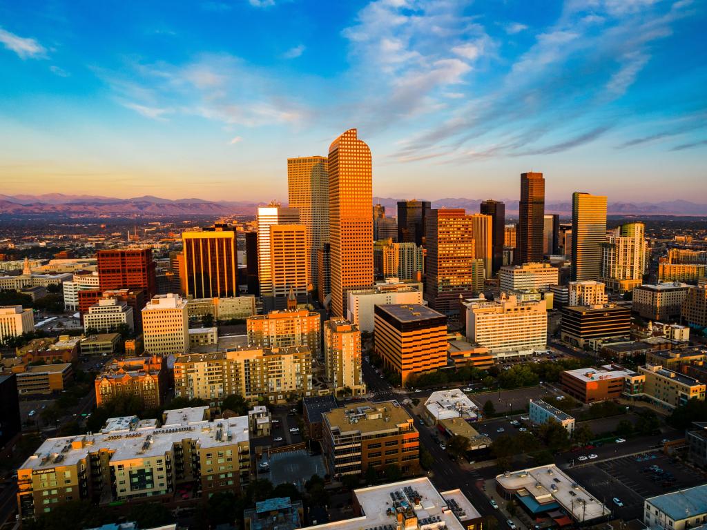 Mile High City, Colorado, USA with a drone view above gorgeous golden hour sunrise in Downtown Denver and the Rocky Mountains in the distance. 