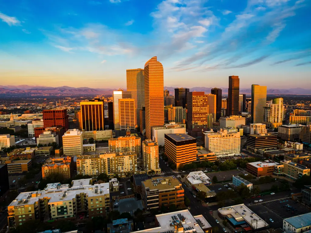 Mile High City, Colorado, USA with a drone view above gorgeous golden hour sunrise in Downtown Denver and the Rocky Mountains in the distance. 