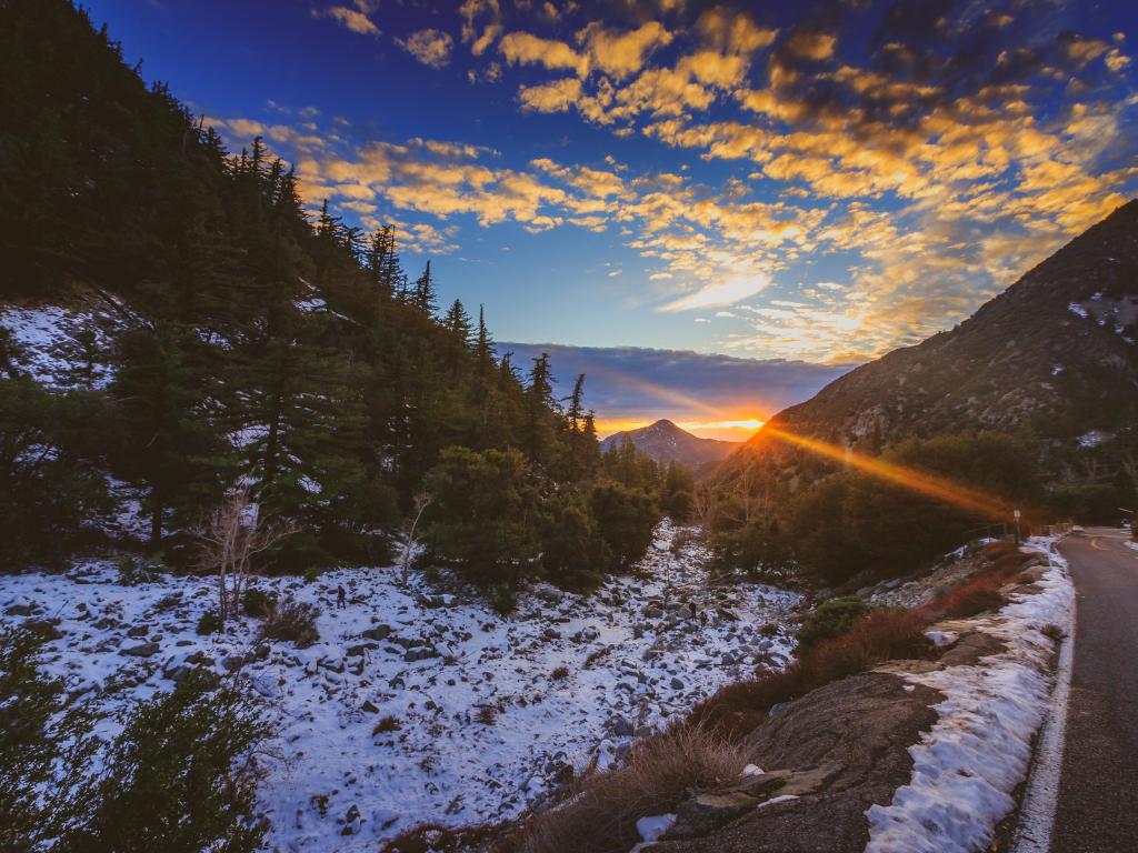Sunset at snow-covered Mount Baldy in winter with a road winding through the tall peaks and colorful clouds in the sky
