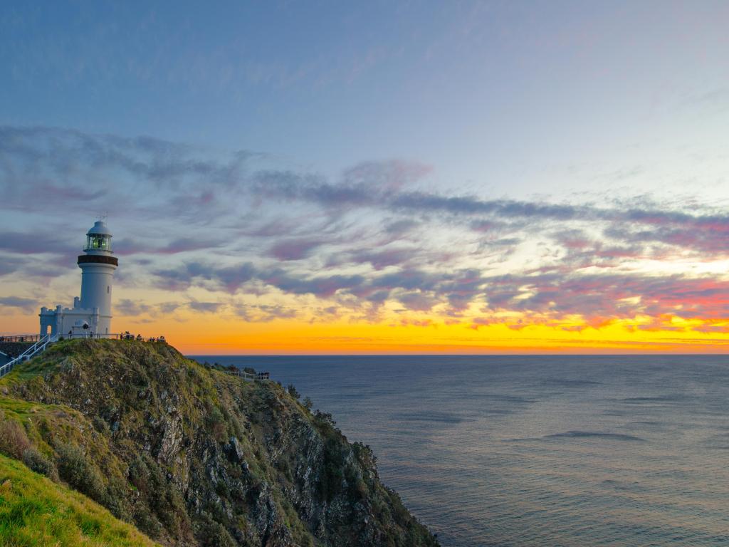 Lighthouse on a cliff overlooking calm sea with gold and pink sunrise light on the horizon