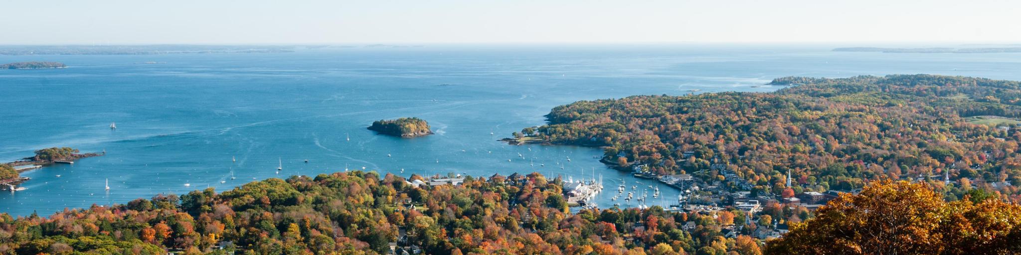Camden Hills State Park, Maine in autumn with a view of the harbour from the summit of Mount Battie in the foreground against a blue sky and the sea in the distance. 