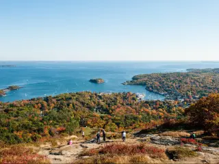 Camden Hills State Park, Maine in autumn with a view of the harbour from the summit of Mount Battie in the foreground against a blue sky and the sea in the distance. 