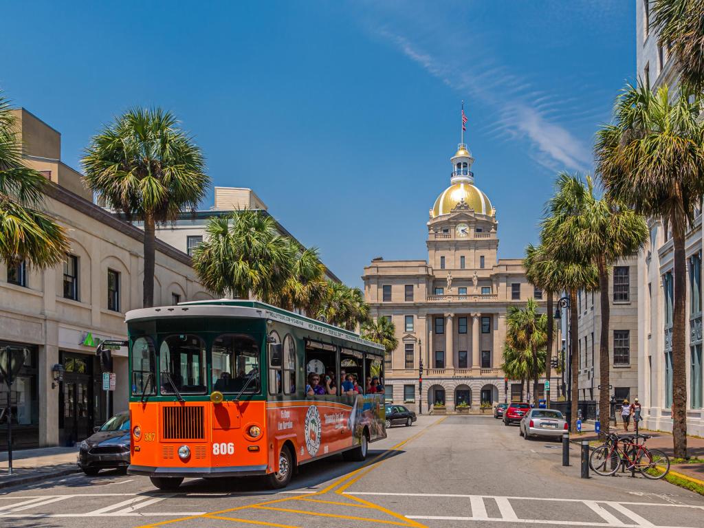 Historic architecture surrounding a traditional Savannah Red Trolley Tour Bus.