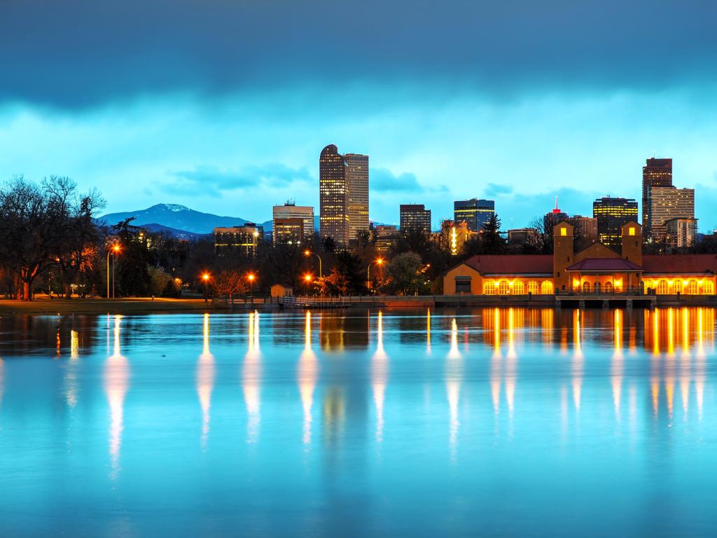City buildings reflected in still lake water in blue early morning light with mountains in the background