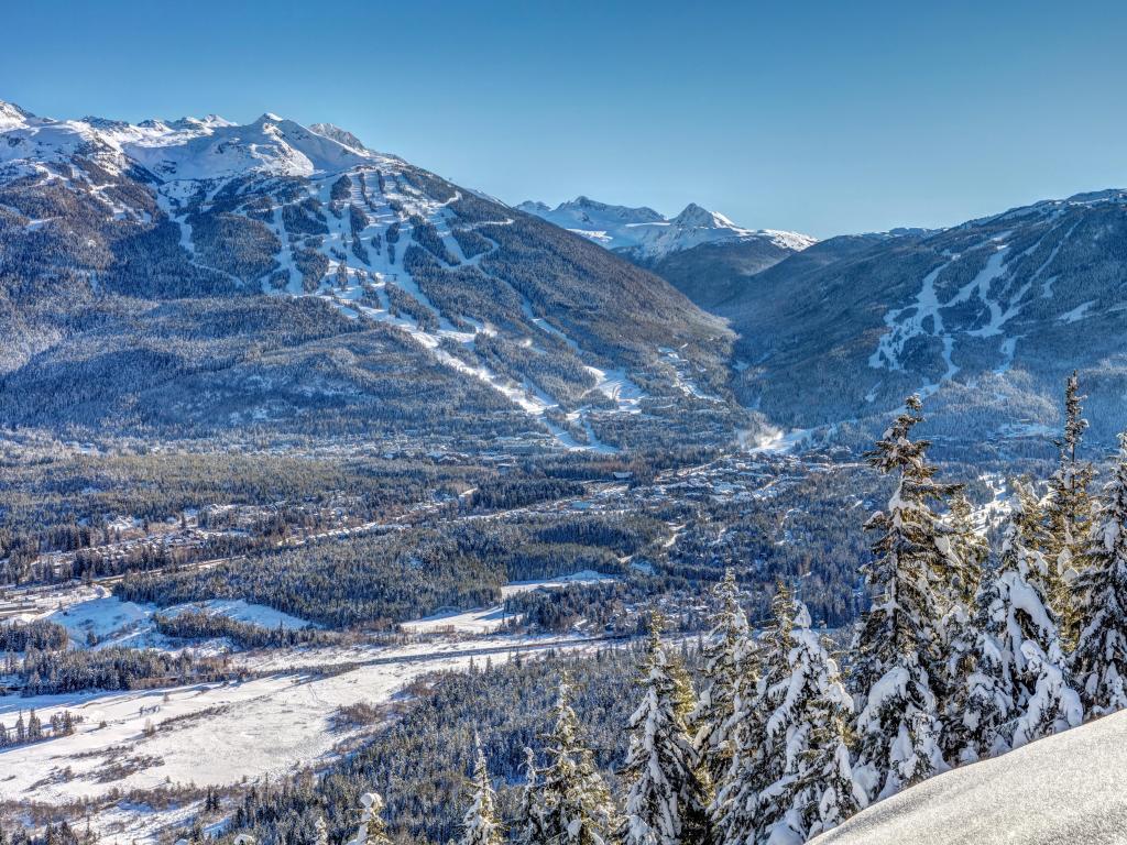 Whistler and Blackcomb Mountains, Canada taken in winter with snow covering the tress in the foreground and the valley and mountains in the distance, taken on a sunny day.