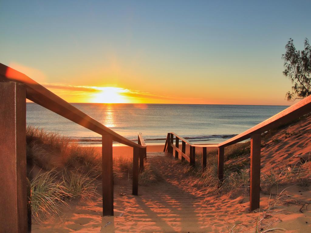 Golden light of sunrise illuminating gold sand beach with wooden steps to the beach over dunes