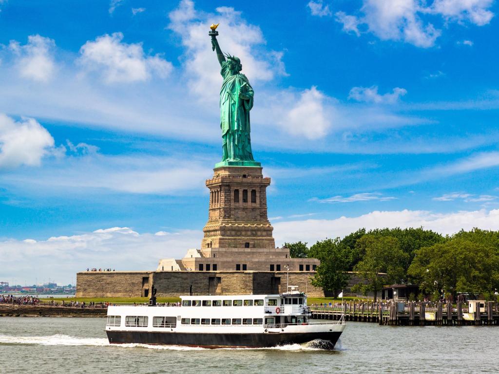 Tourist boat near the Statue of Liberty on a sunny day with some clouds