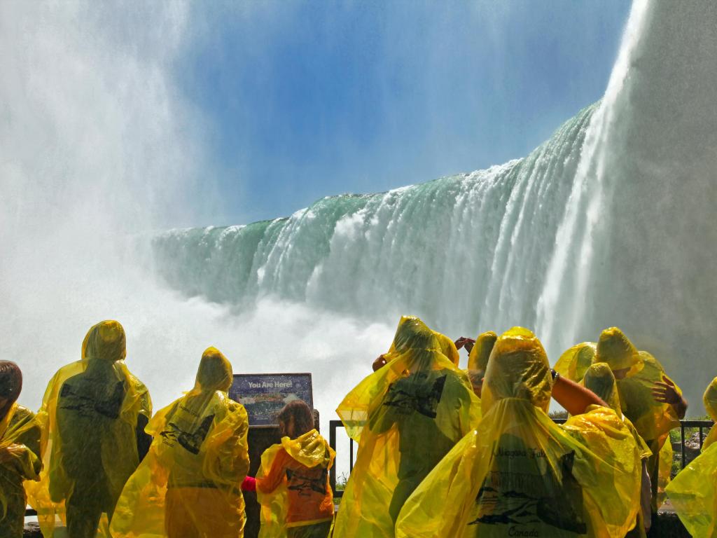 Tourists wearing yellow waterproof tops near the falls on the Canadian side on a sunny day