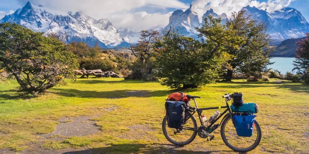 A bike packed with things parked in front of trees and green trees and snowy mountains 