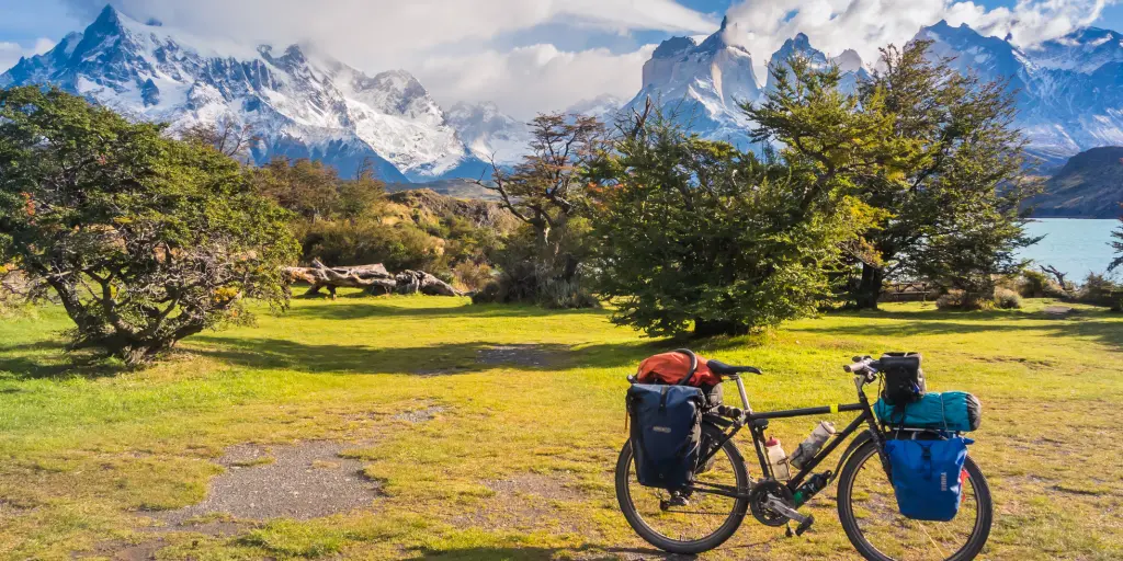 A bike packed with things parked in front of trees and green trees and snowy mountains 