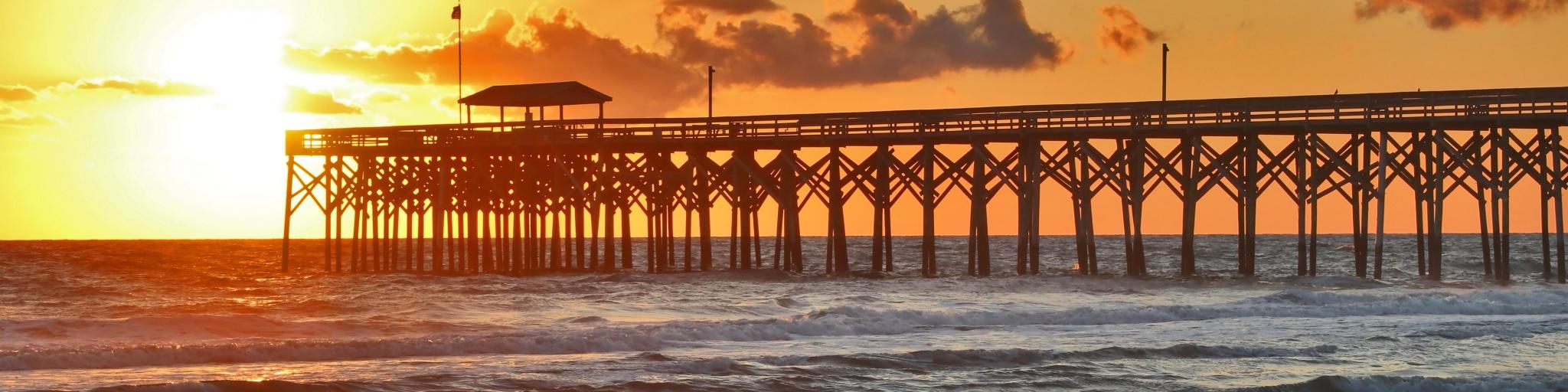 Myrtle Beach, South Carolina, USA with a golden sunrise over calm Atlantic ocean beach with wooden pier. 
