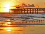Myrtle Beach, South Carolina, USA with a golden sunrise over calm Atlantic ocean beach with wooden pier. 