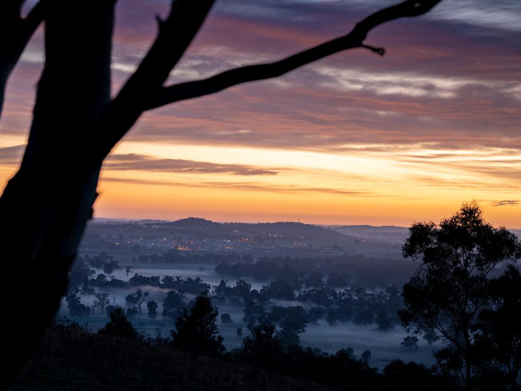 Misty sunrise view across fields with low rise lights of the city of Wagga Wagga in the distance