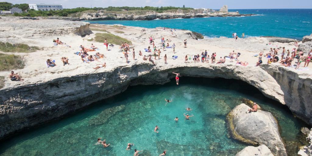 People jumping into the blue water of Grotta della Poesia, Puglia