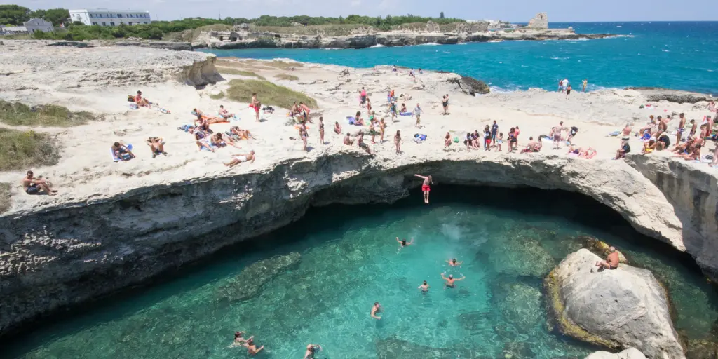 People jumping into the blue water of Grotta della Poesia, Puglia
