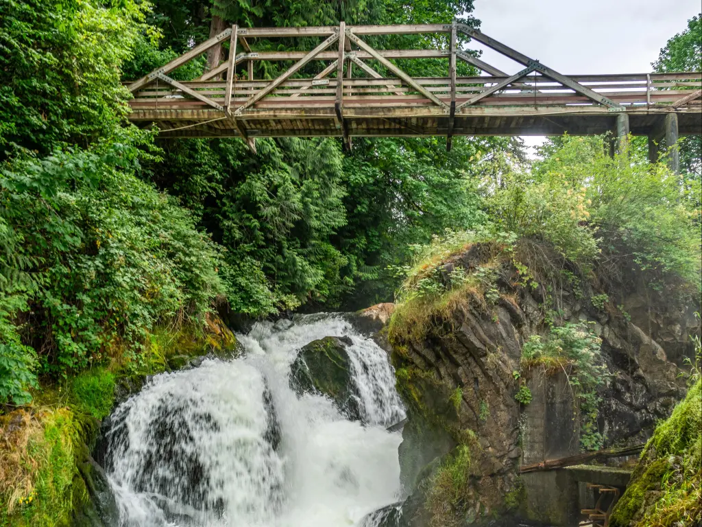 Water explodes through the lower section of Tumwater Falls, with wooden viewing bridge above the waters