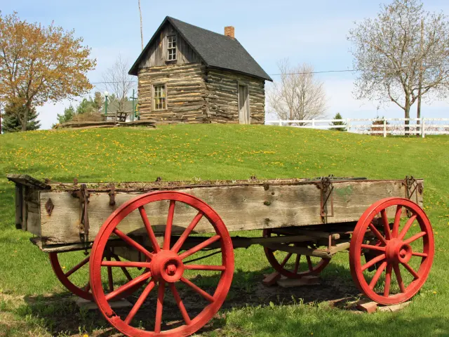 Farm estate with a red-wheeled pioneer wagon and restored log cabin  in the background