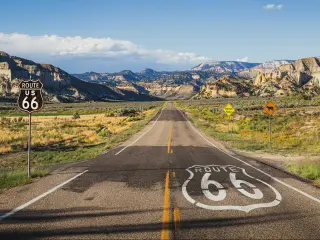 Section of iconic Route 66 stretching towards the horizon and mountains in the background, with a Route 66 road sign 