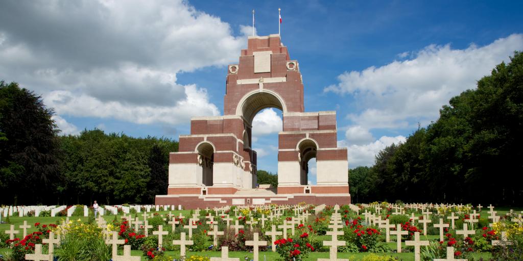 The brickwork arches of the Thiepval Memorial, France, with rows of crosses and red flowers in front