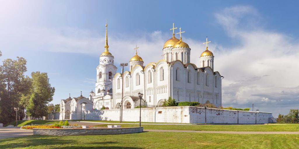 The outside of the white-stone Holy Dormition Cathedral in Vladimir, Russia,  with its golden roofs looking bright, on a sunny day